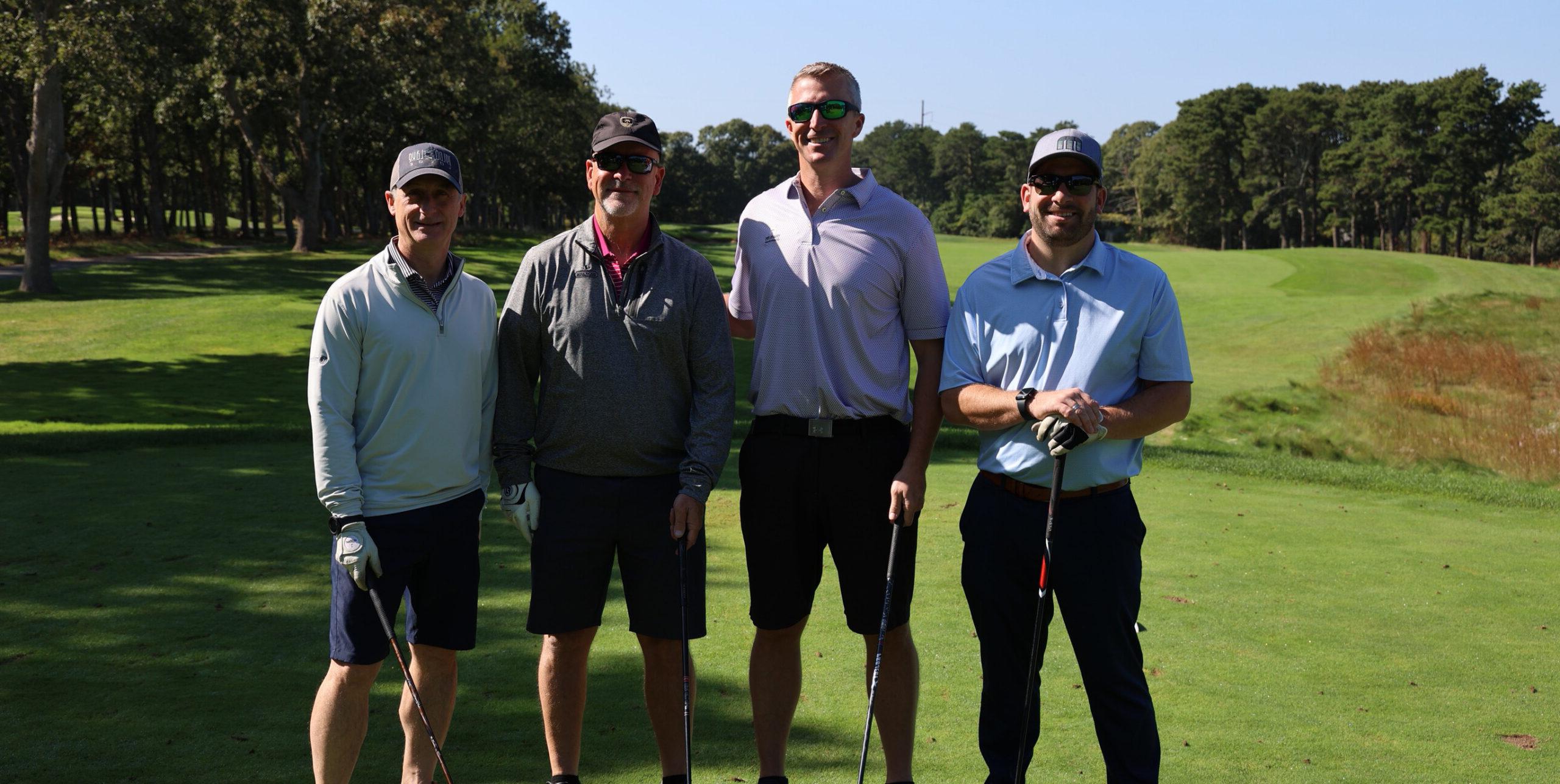 4 people standing with golf clubs on a golf course.